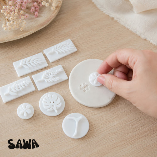 Hand pressing a Sawa floral stamp into a white air-dry clay disc
