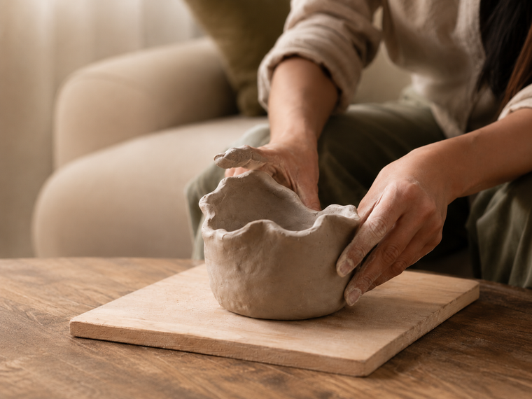 Close-up of hands shaping a clay pinch pot on a wooden board