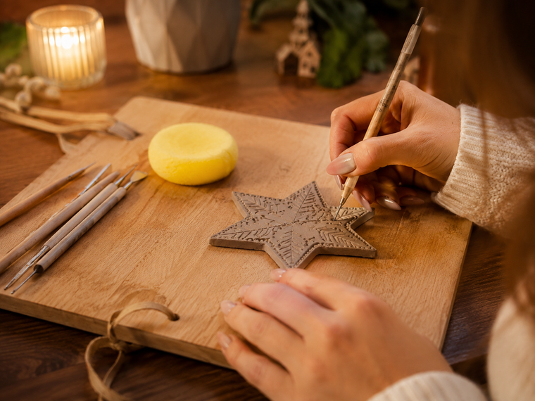 Hands carving a clay star ornament on a wooden board in the evening